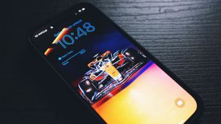 A close up of an iPhone 14 with vibrant wallpaper displaying a Formula One car.