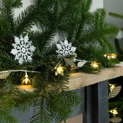 Close up of fir garland with fairy lights and snowflake decorations