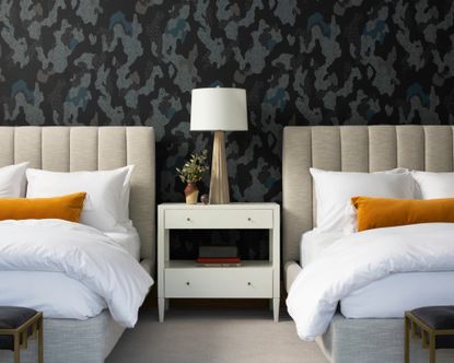 twin bedroom with cream beds, orange pillows and dark gray camouflage wallpaper 