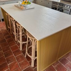 Kitchen island with white top and yellow patterned sides, with rattan bar stools, on tiled terracotta floor