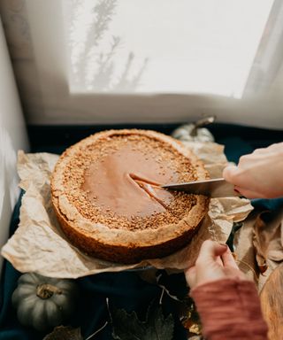 A caucasian woman cutting a homemade pumpkin pie spice cheesecake portion with a knife