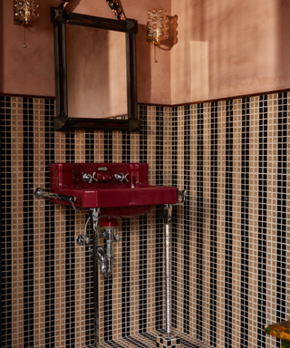 Tile bathroom walls in salmon and black with vintage red sink and brass exposed piping