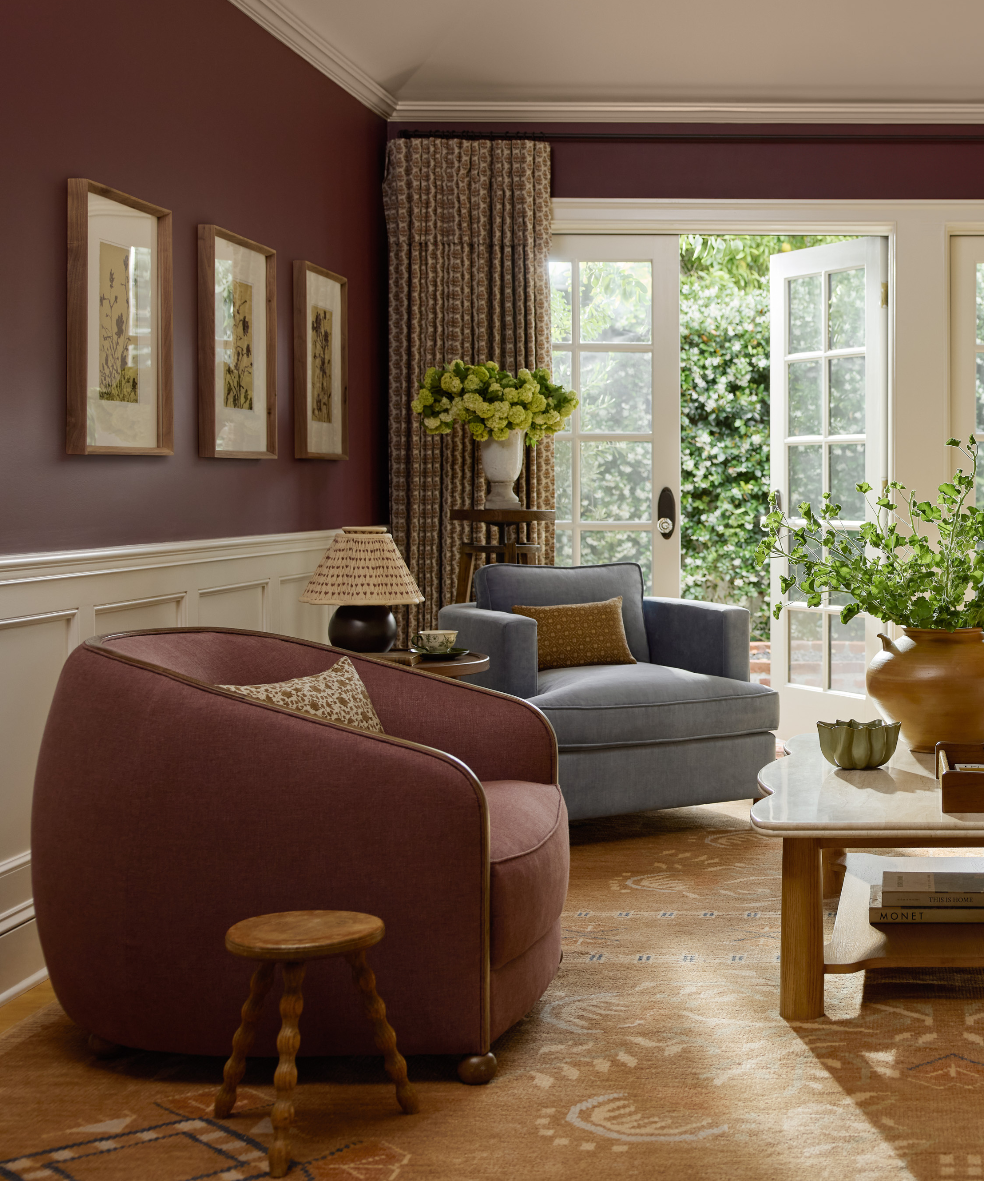 a cozy living room with a maroon chair, a tan rug, a blue accent chair, and maroon painted walls