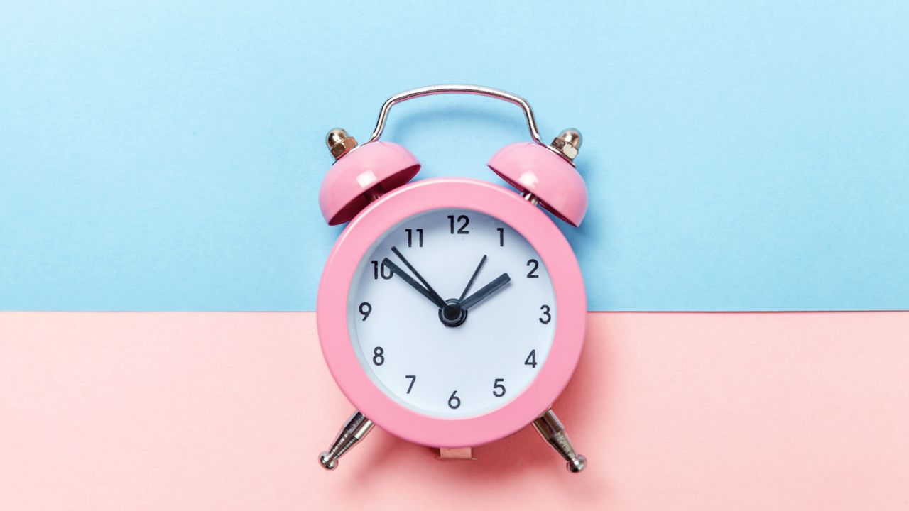 pink alarm clock on blue and pink background 