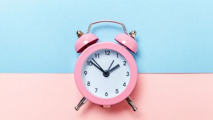 pink alarm clock on blue and pink background 