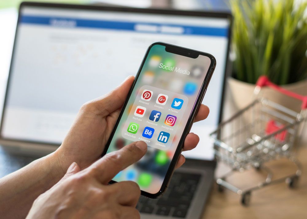 An iPhone X being used with a MacBook Pro in the background.