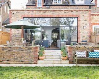 An example of sloping garden ideas showing a how with a rear extension leading onto a patio area with a parasol and a wooden bench