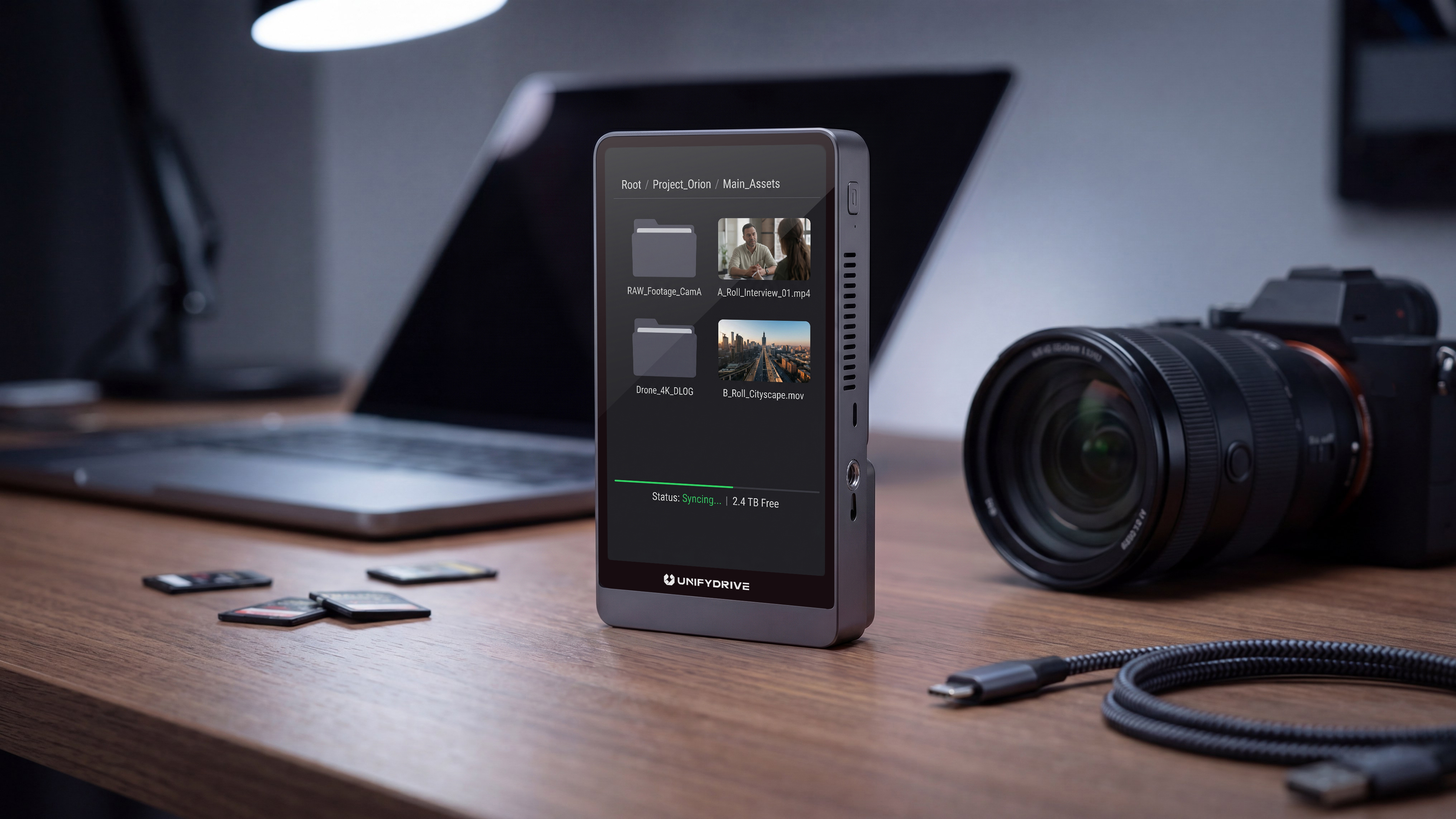 The UnifyDrive PixelMob sits on a desk with a laptop, camera, and SD cards