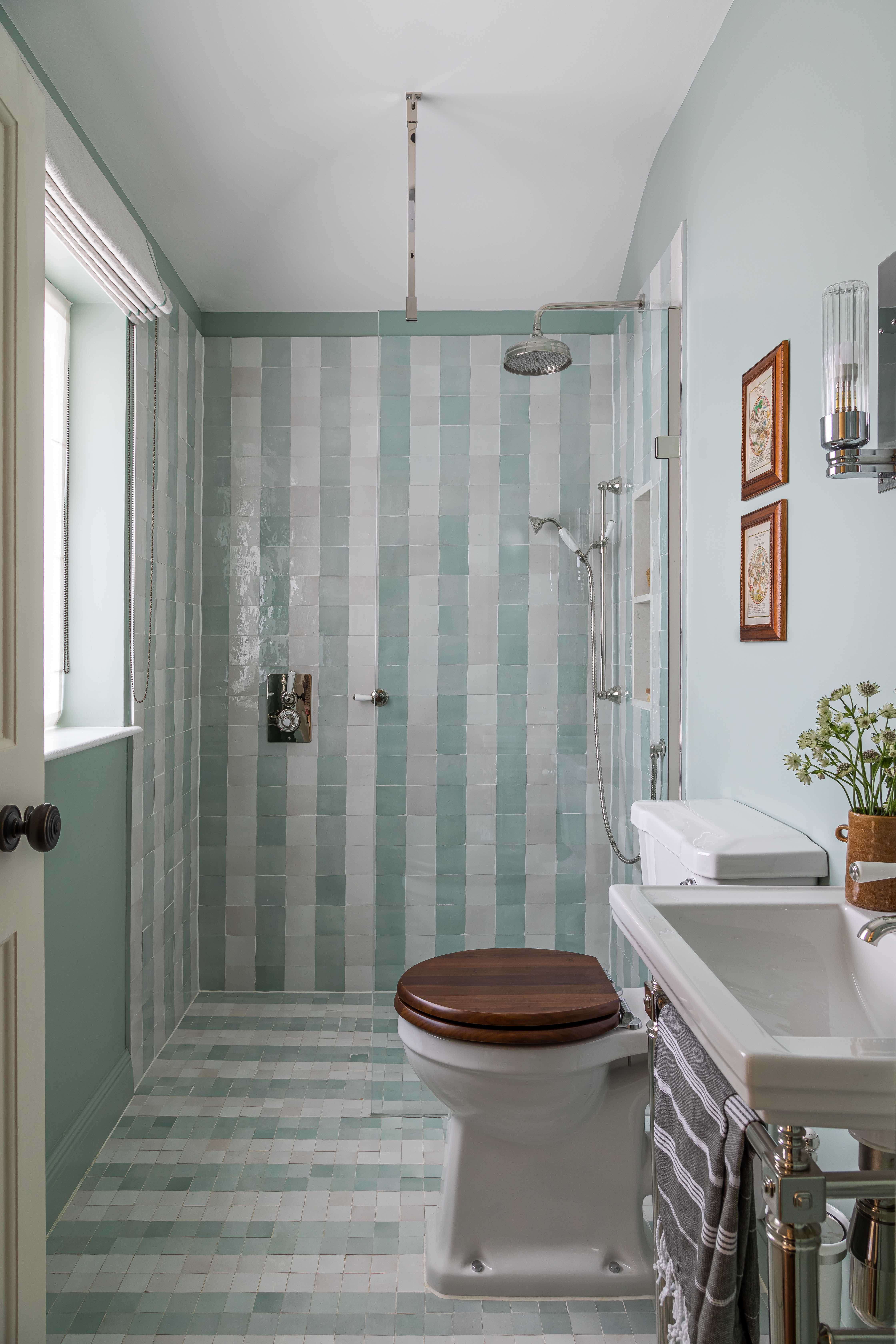 bathroom with striped white and light green zellige tiles. There is also a toilet in the middle of the space with a sink installed