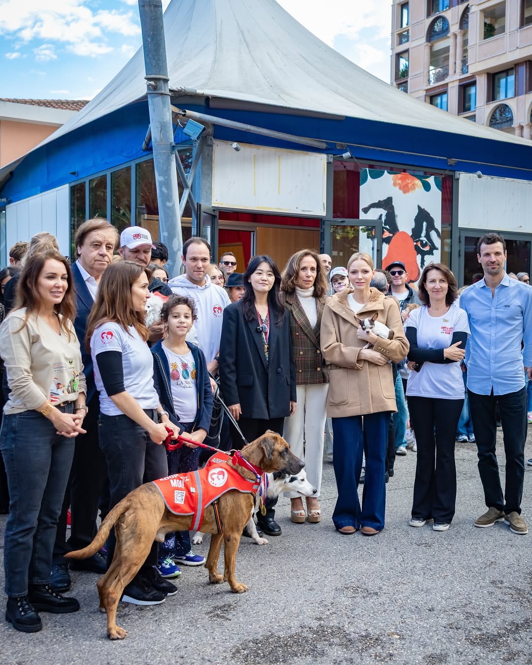 Princess Charlene holding a dog posing with a group of people and dogs