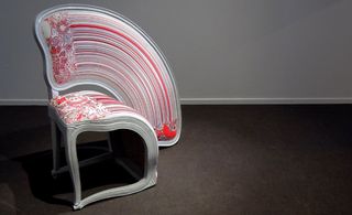 View of 'Lathe V' by Sebastian Brajkovic - a grey and red chair with a rainbow style backrest that continues down one side of the chair