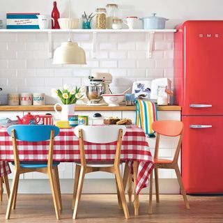 kitchen with wooden dining table with red gingham tablecloth, white tiles and red Smeg fridge