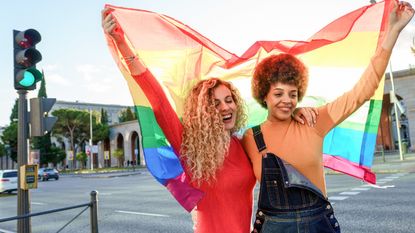 LGBTQ+ ally Lesbian women couple in the city with gay pride rainbow flag - stock photo