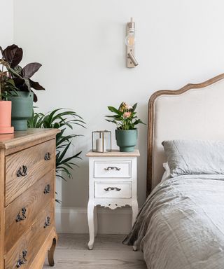 A white bedroom with a white bed, nightstand, brown drawers, and plants