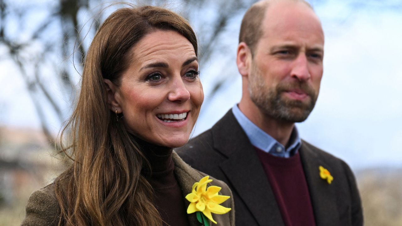 Kate Middleton and Prince William standing in front of a bare tree smiling and wearing daffodil pins