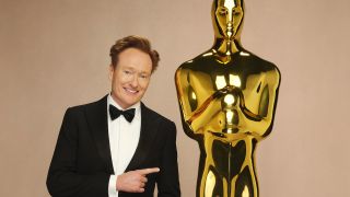 Conan O'Brien in a tux next to giant Oscar statue for 2025 Academy Awards