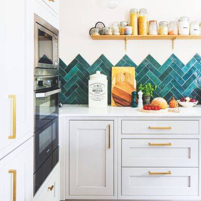 Kitchen with white painted walls and blue chevron tiles as a splashback. The kitchen cabinets are grey with gold hardware