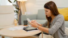 A college student works with a calculator and a tablet while sitting at table at home.