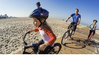 GOPRO helmet mount is shown on a child's helmet while she rides her bike with two adults behind her on bikes.