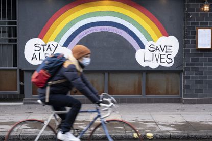Person cycling past rainbow painted on wall during UK lockdown 3.0