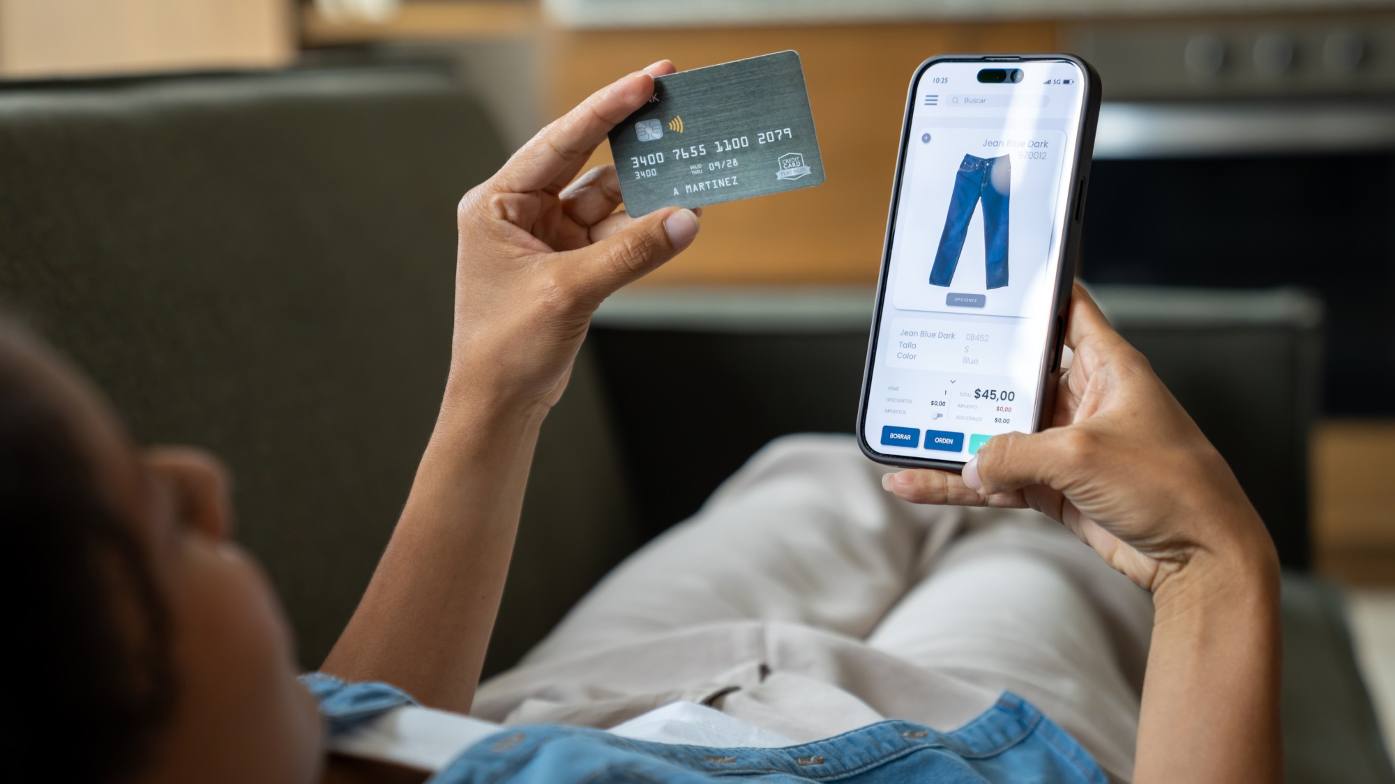 A woman holds a credit card in one hand and a smartphone showing a clothing website in the other