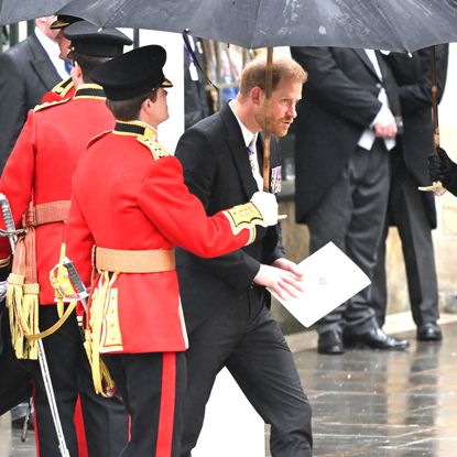Prince Harry walking under an umbrella