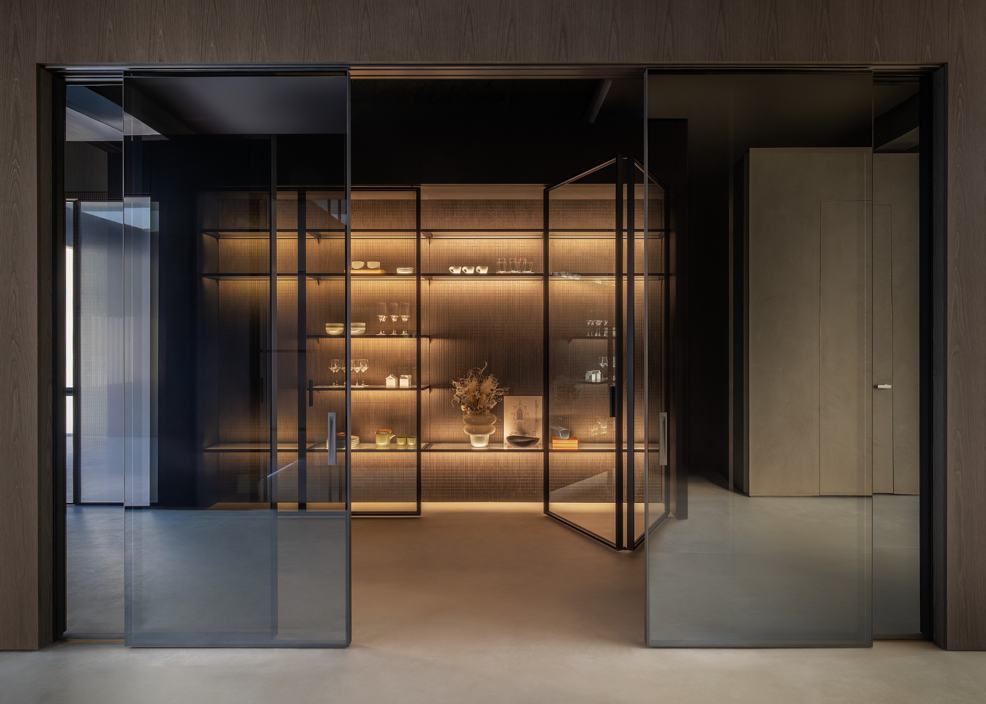 A set of sliding doors revealing a set of glass doors opening into a room of shelves with soft lighting