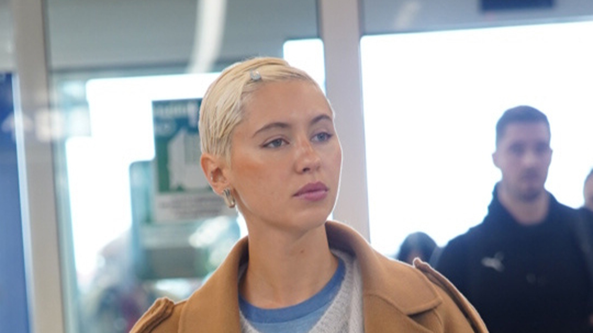 Iris Law wearing a tan coat, gray cardigan, beige jeans, blue sneakers, and a lime Louis Vuitton Speedy bag.