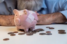 Broken piggy bank taped together sitting on a table in front of hands.