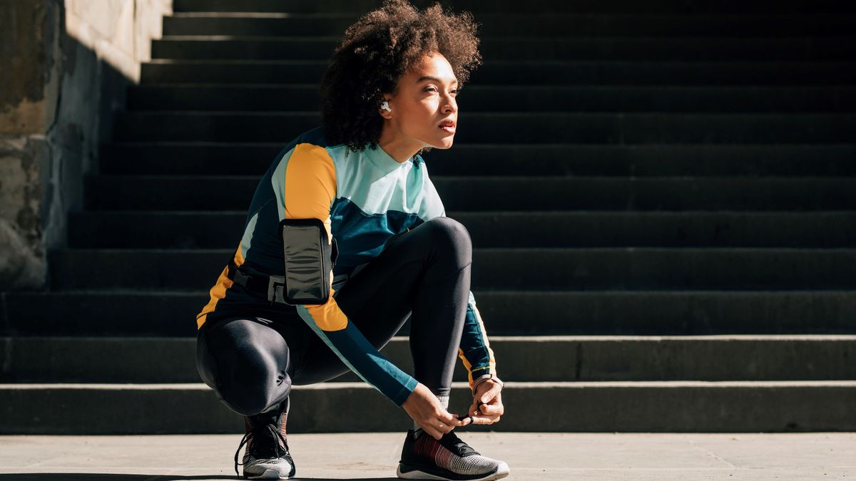 Woman tying running shoes wearing wireless earbuds