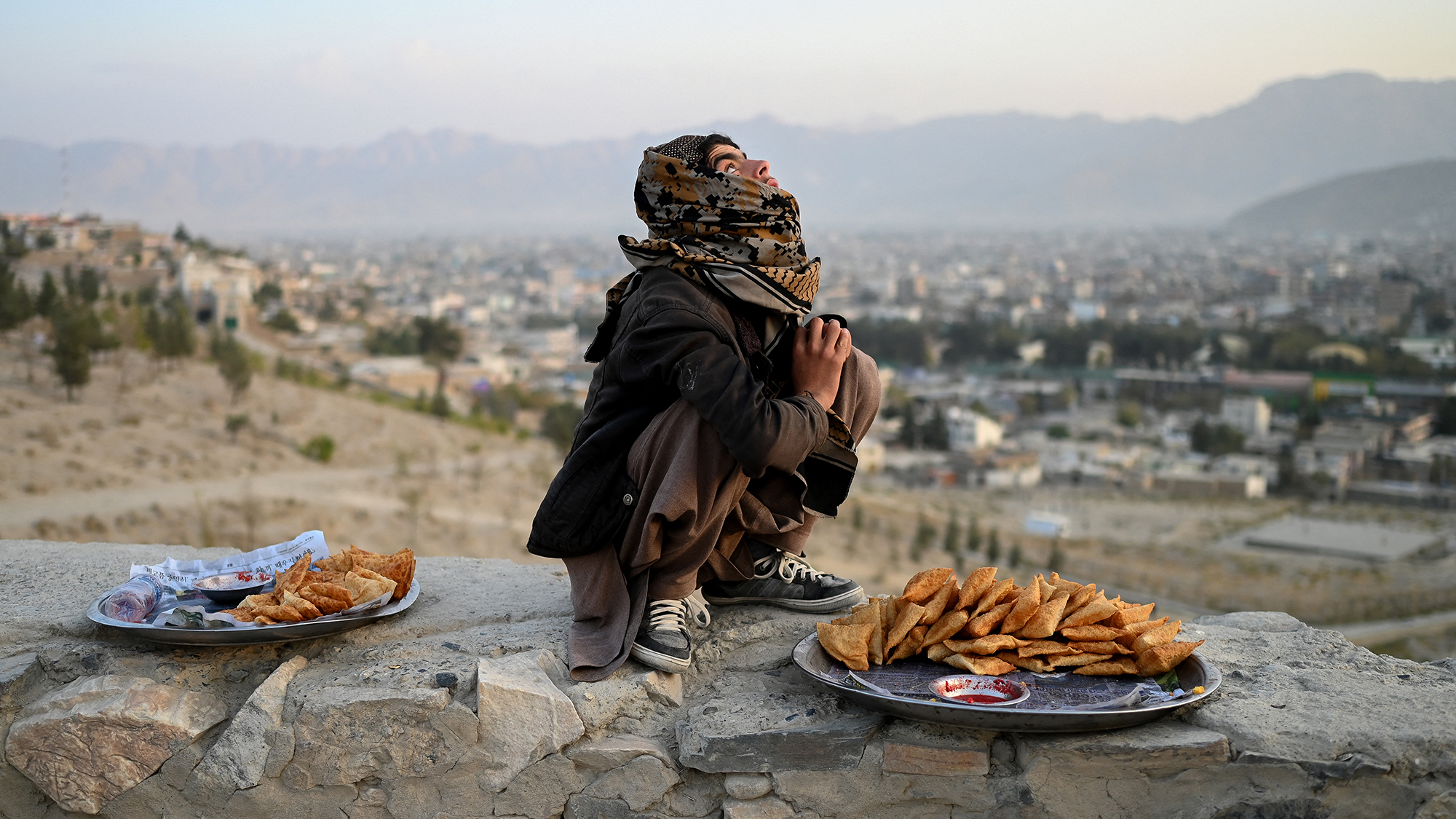 An Afghan samosa vendor looks on as people fly kites at the Nadir Khan hilltop overlooking the city of Kabul, Afghanistan
