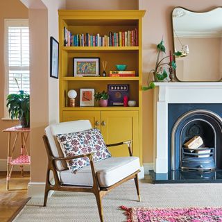 yellow bookcase, chair with cushion and ornate fireplace