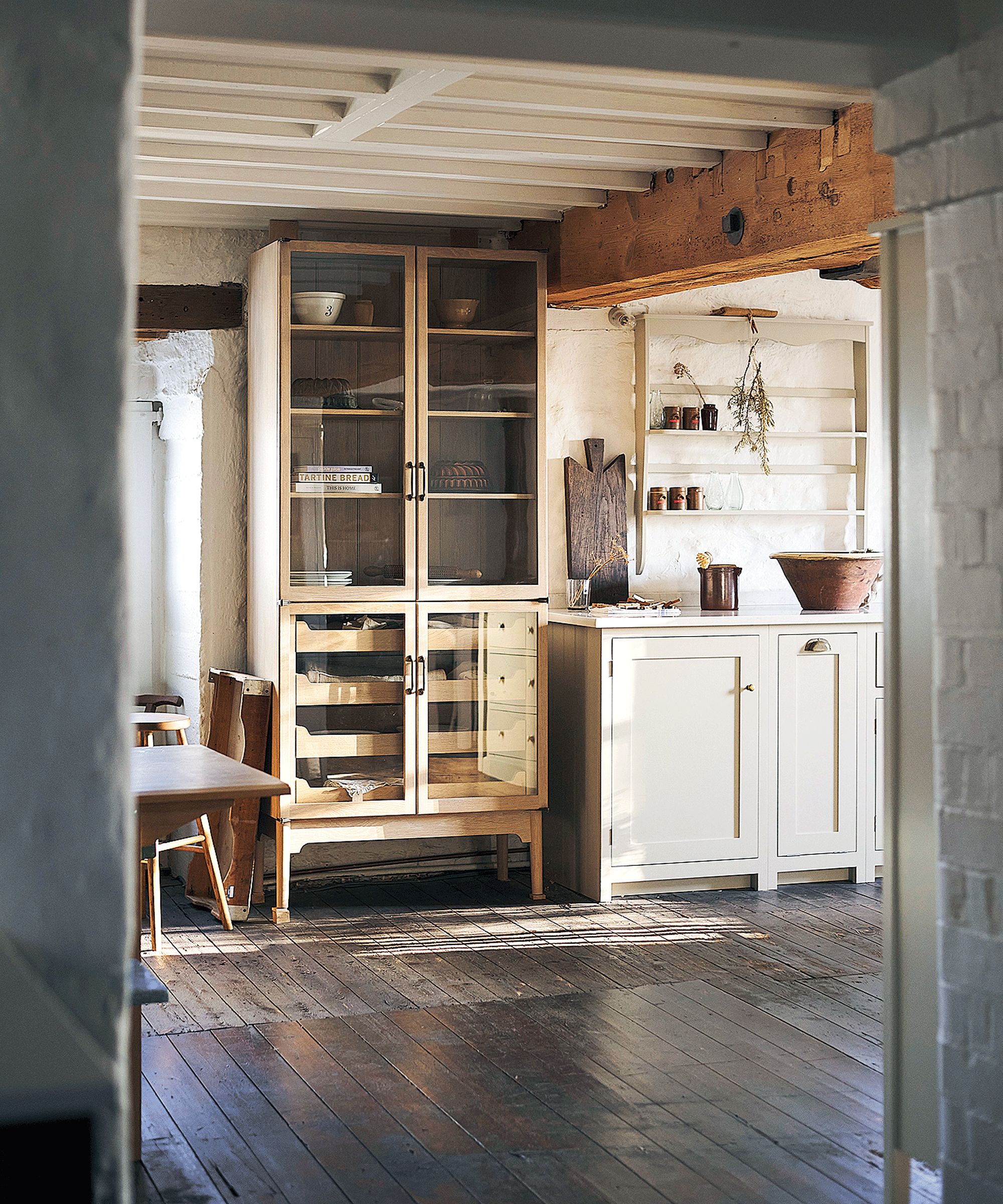 A glass freestanding kitchen cabinet in a kitchen with dark floor boards