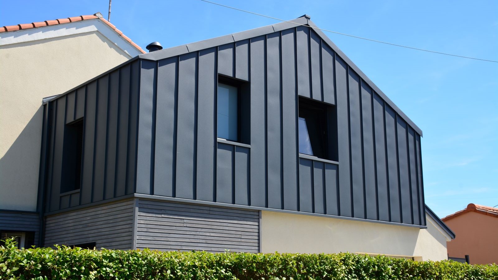 A dark grey clad extension with two windows and beige render underneath and behind