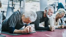 Three seniors in a gym in a row performing the plank exercise. One man is resting on the floor, unable to continue