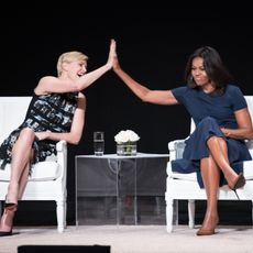 Charlize Theron and Michelle Obama high five across a table.