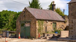 A stone built garage with green double garage doors and a pitched roof