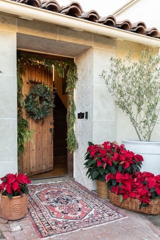 Christmas door decor with wreath and garland around the door frame, antique rug, baskets and a pot full of poinsettia