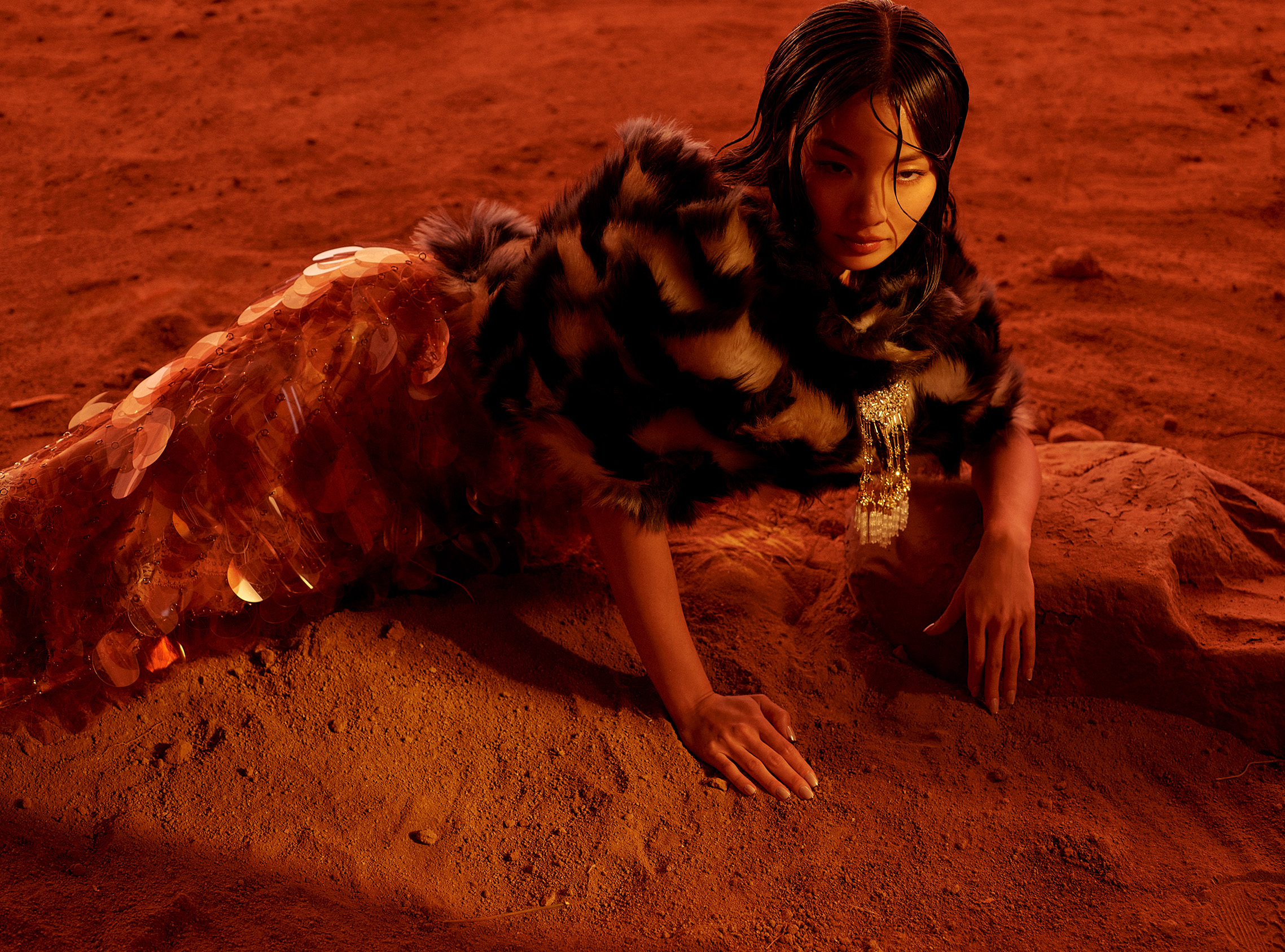 Anna Sawai reclines on red desert rocks in a dark textured top and a shimmering skirt.