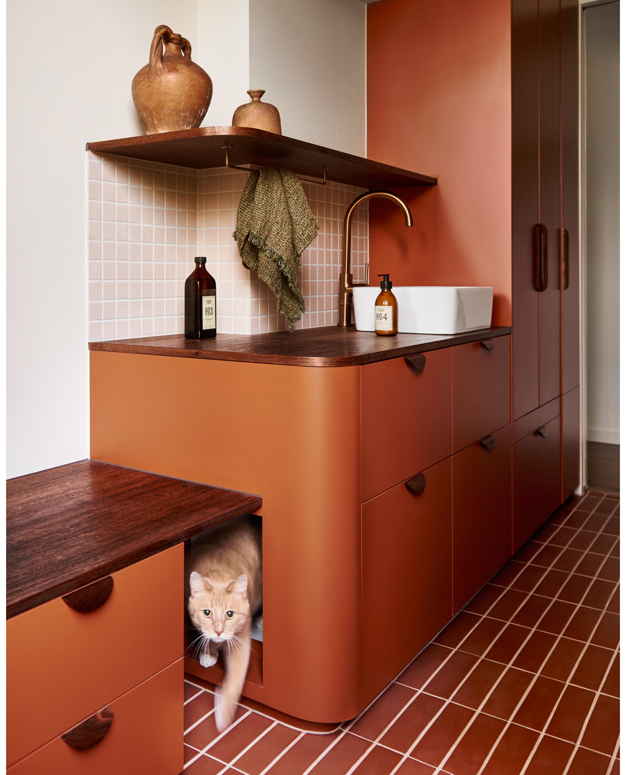 A rust orange laundry room with a tiled floor and wooden work tops and a built in litter box, tucked into the cabinets.