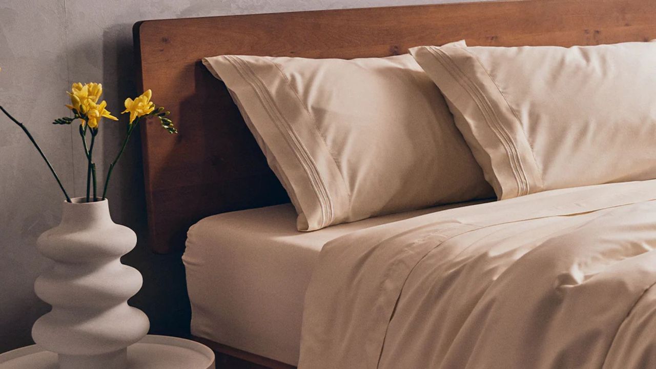 Mellanni sheets on a bed against a gray wall beside a nightstand with a vase of yellow flowers. 