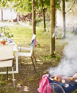 Outside garden scene with table and chairs, bbq, string lights on tree