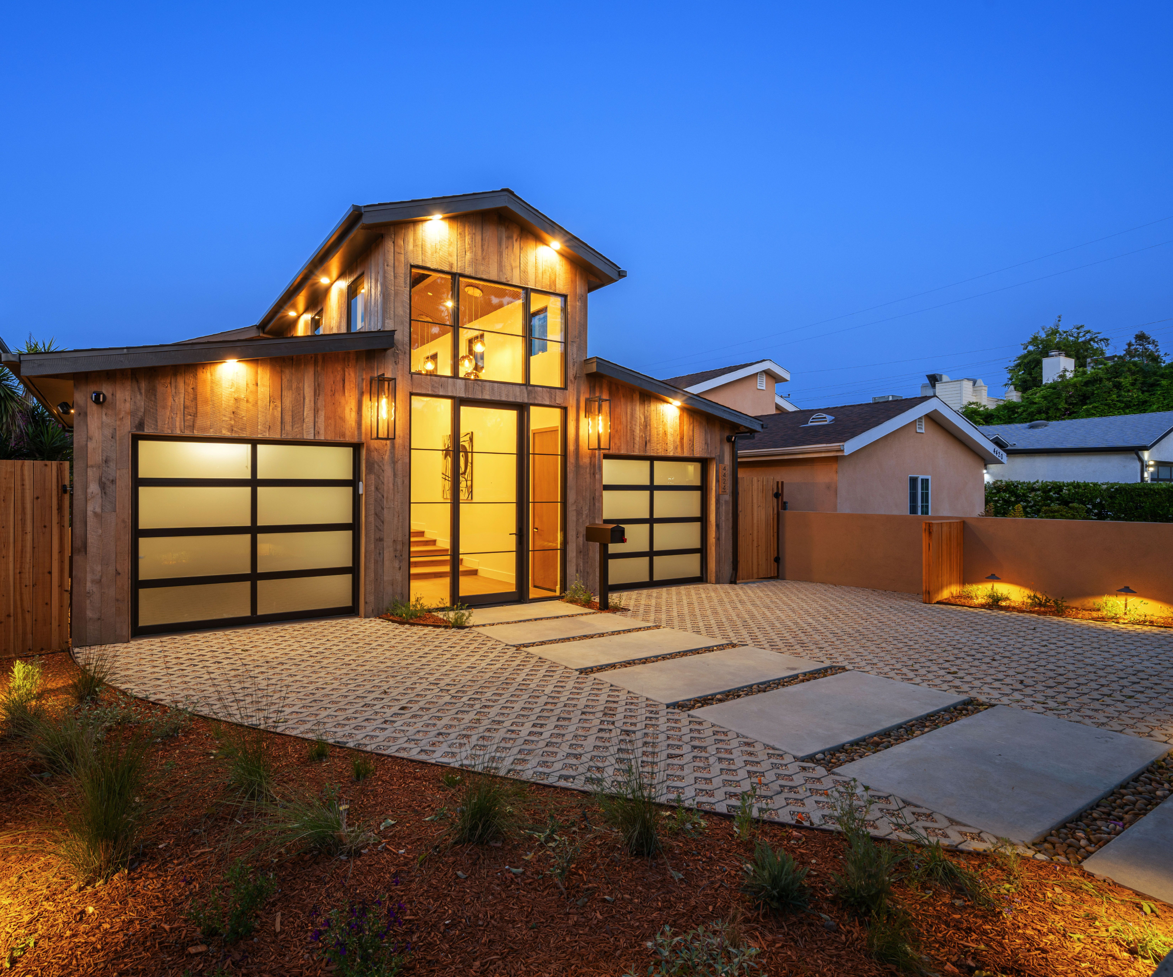 exterior view of timber clad modern house with sloped driveway. lighting on driveway and house