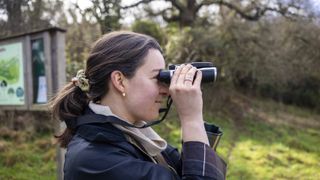 A female photographer holds the Camonity 5M 2" LCD 16GB Digital Binoculars in her hands in a sunny field