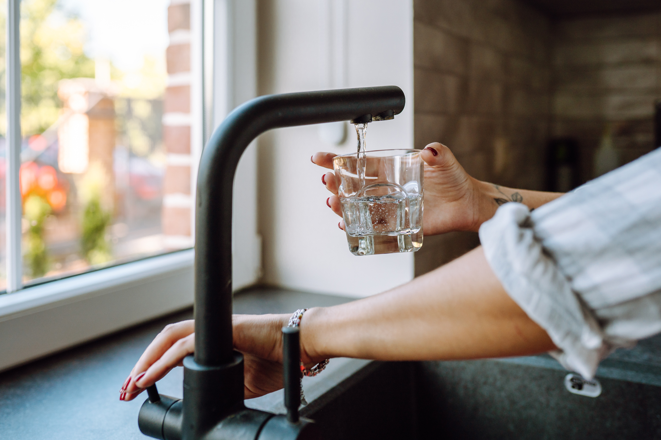 A person using a black kitchen tap to pour themselves a glass of water.