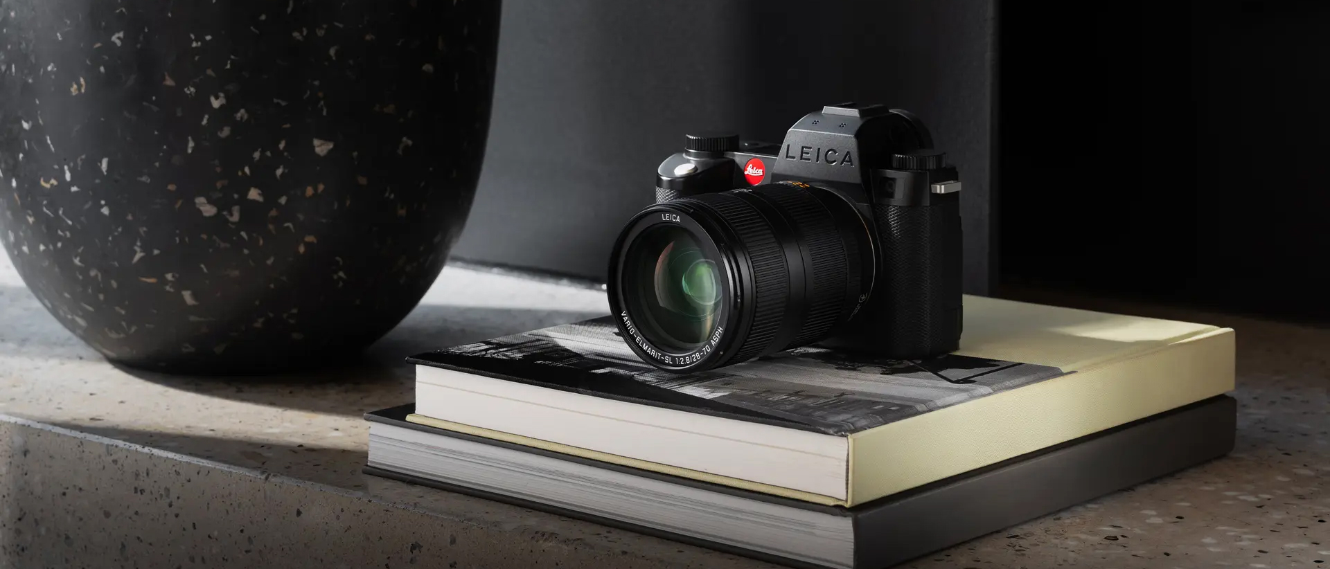 The Leica Vario-Elmarit-SL 28-70mm f/2.8 lens mounted on a camera sitting on a pile of books