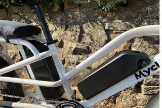 The Mycle Cargo Electric bike with twin batteries is shown close up here in the centre and rear of the bike frame which is in front of a stone wall.