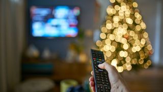 A person using a remote in front of a television and Christmas tree