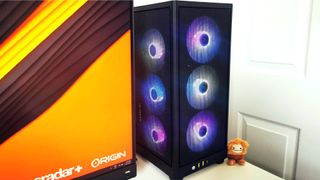 Origin Chronos V3 PC with rainbow RGB lights on white desk next to monitor