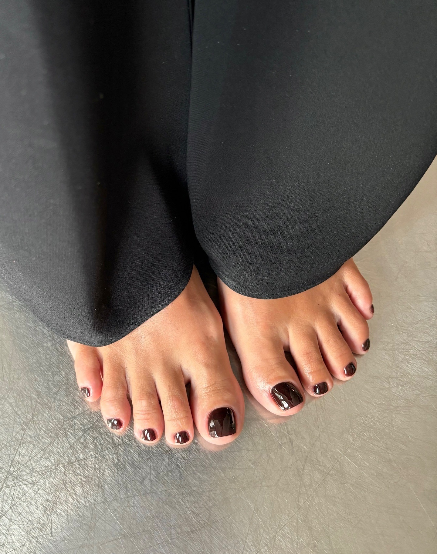 Piedi di una donna su un pavimento argentato con pedicure color bordeaux